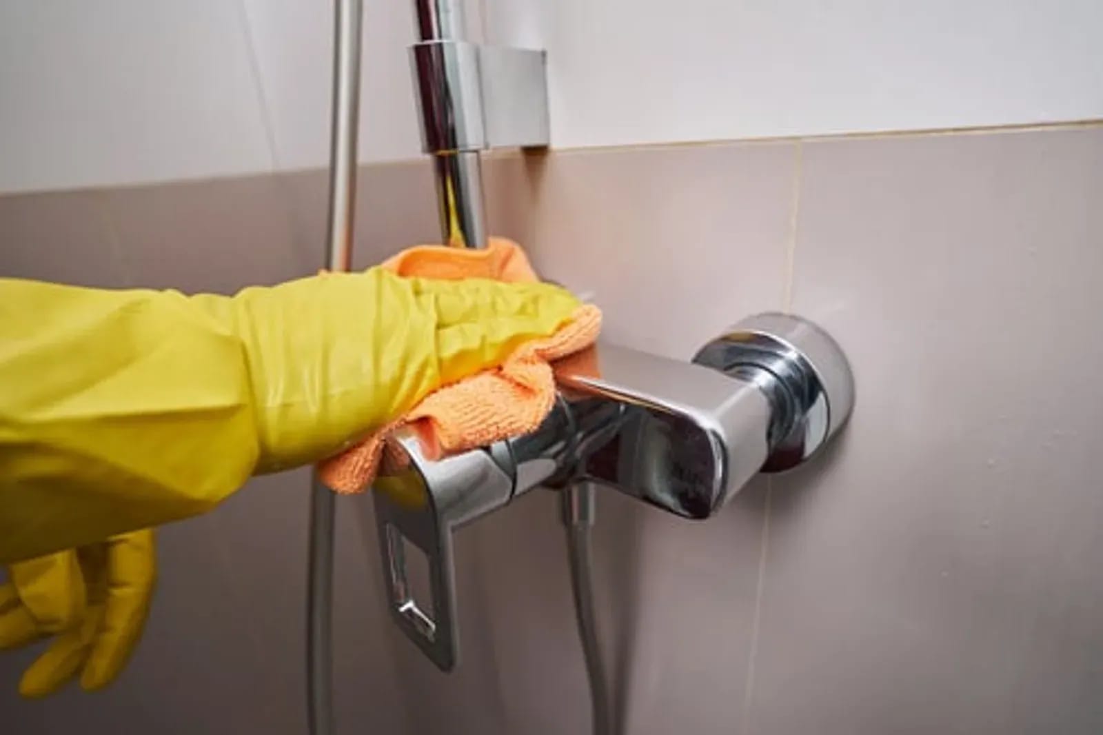 Gloved hand polishing a chrome shower fixture with an orange microfiber cloth