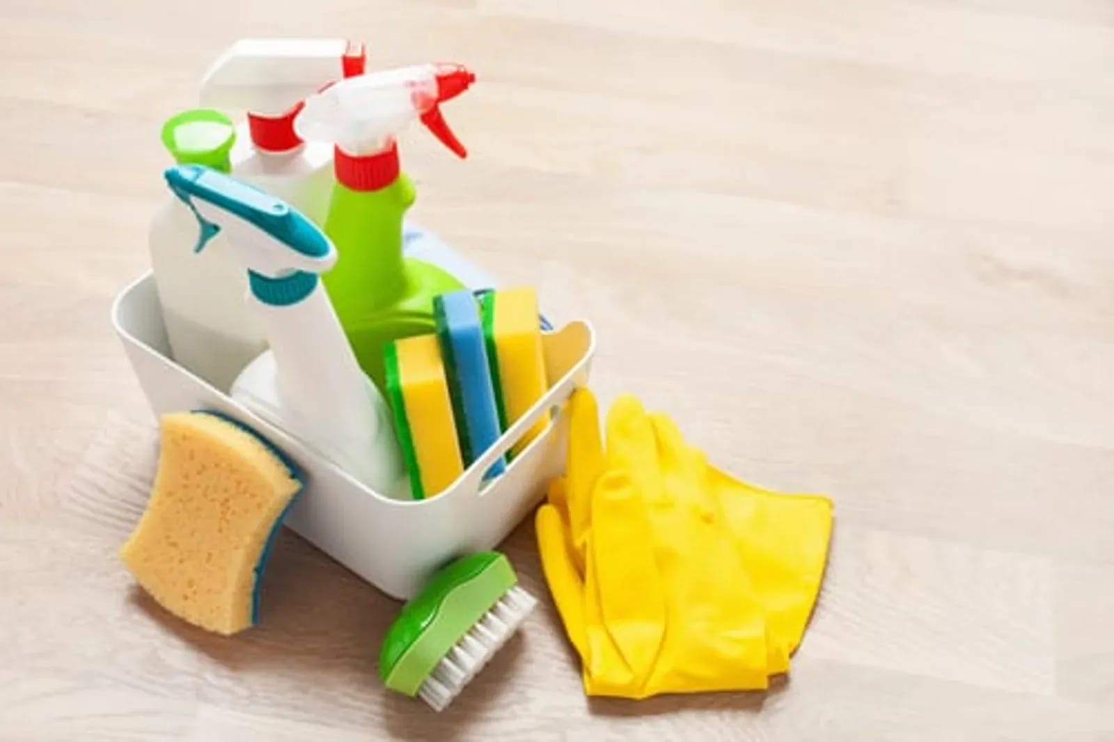 White caddy of cleaning supplies and a scrub brush arranged neatly on a light wood floor