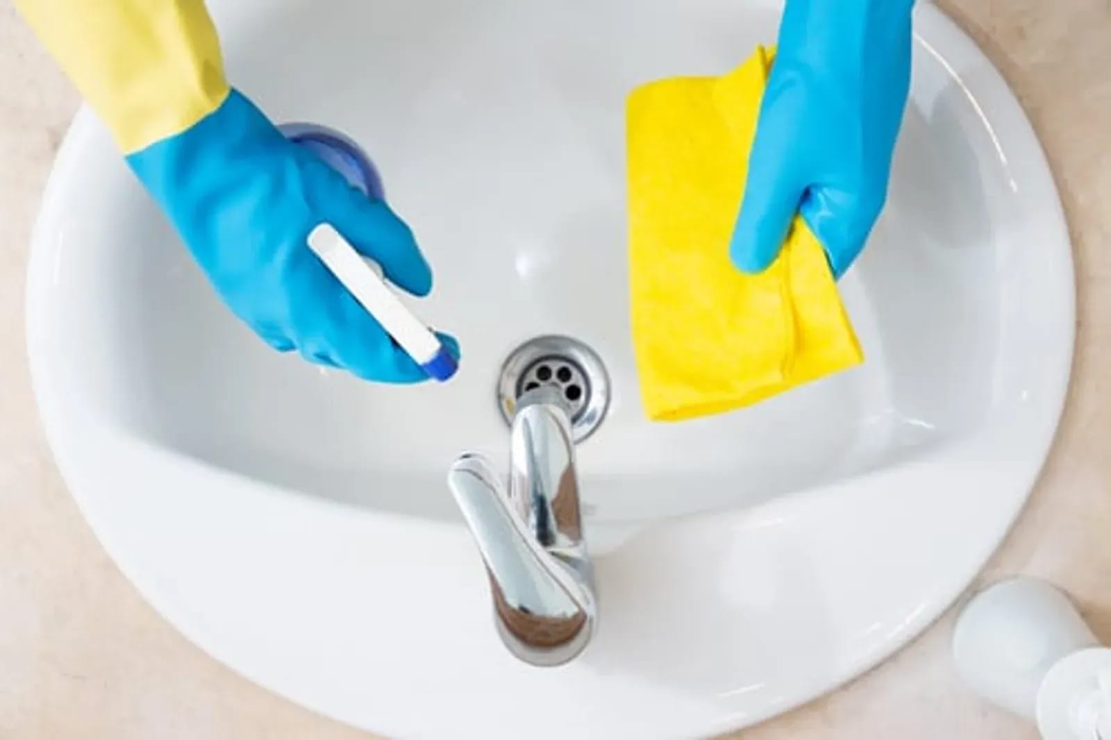 Gloved hands scrubbing a bathroom sink and fixtures during a deep cleaning service in Greater New Orleans