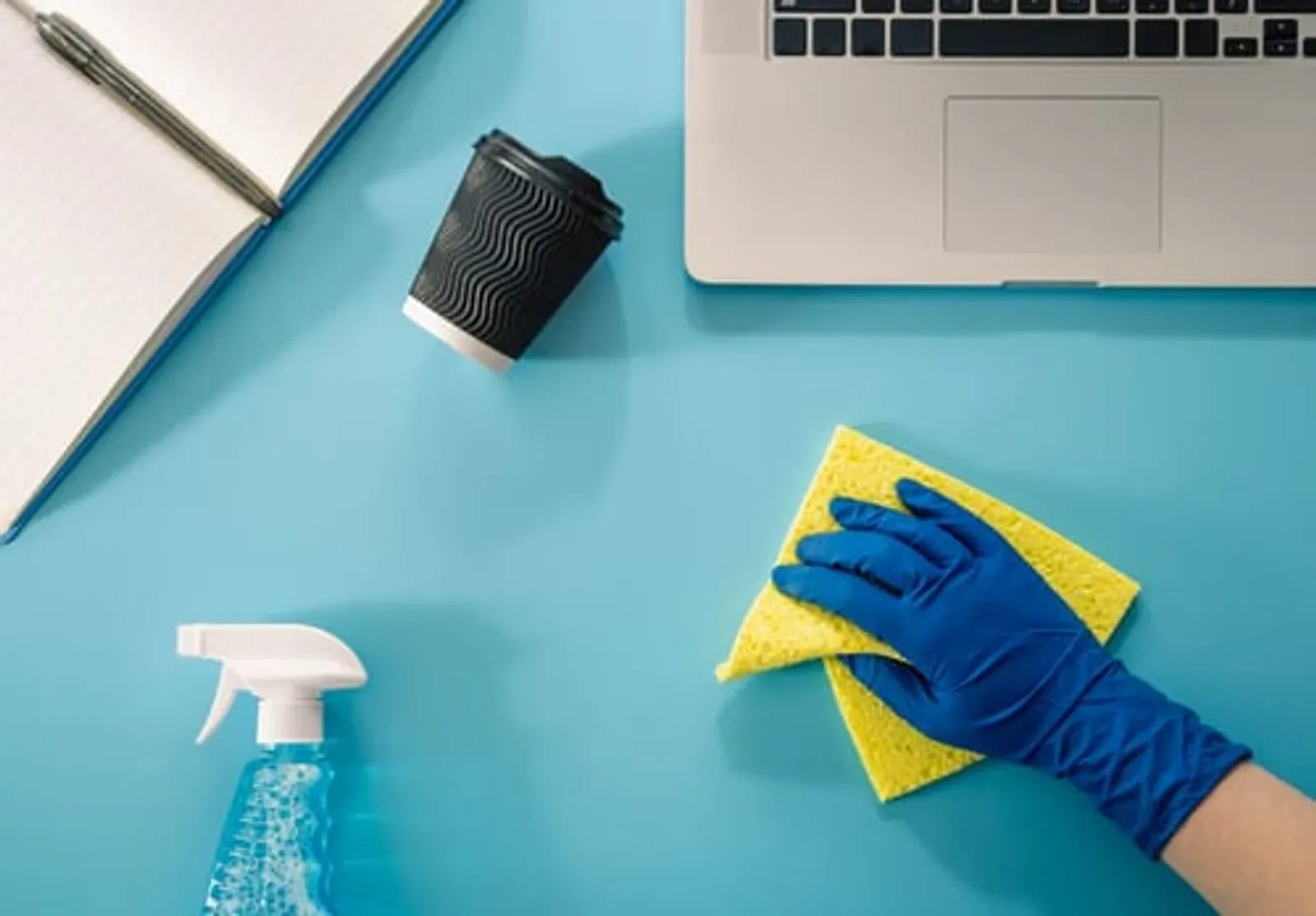 Gloved hand disinfecting an office desk beside a laptop during commercial cleaning service